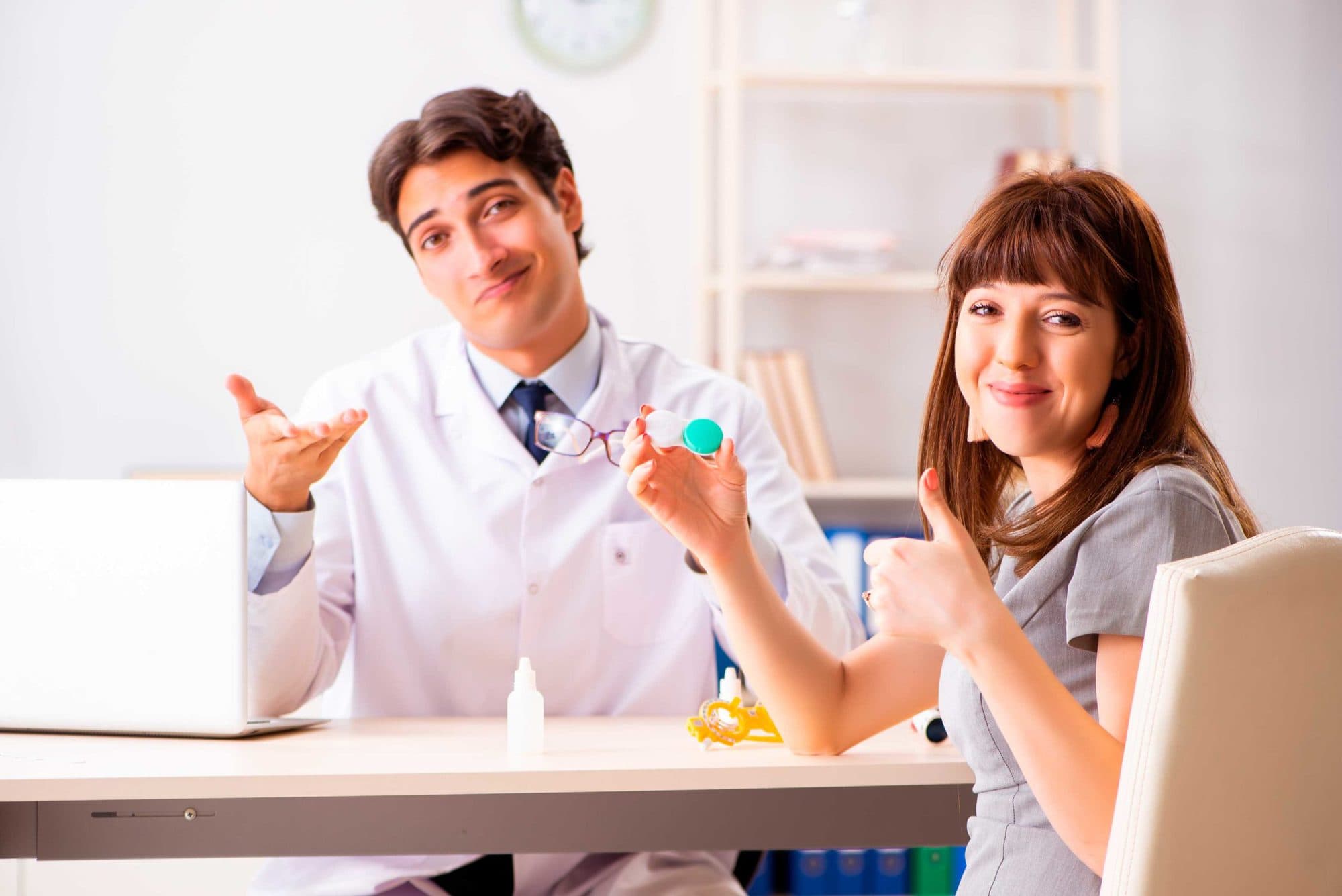 Mitarbeiter und Frau sitzen am Tisch und Frau hält Kontaktlinsenbehälter in der Hand